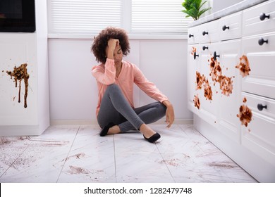 Portrait Of A Sad Young Woman Sitting On Floor With Spilled Food On The Kitchen