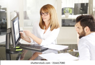 Portrait Of Sales Team Analyzing Financial Data. Middle Age Businesswoman And Young Assistant Consulting While Sitting At Office In Front Of Computer. 