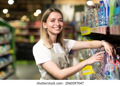 portrait of saleswoman, woman smiling and looking at camera in supermarket. Pleasant friendly female seller standing in the store between the rows . Trade business and people concept