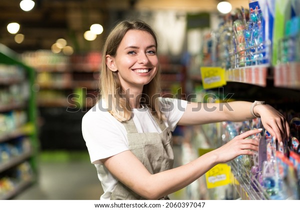 portrait of\
saleswoman, woman smiling and looking at camera in supermarket.\
Pleasant friendly female seller standing in the store between the\
rows . Trade business and people\
concept