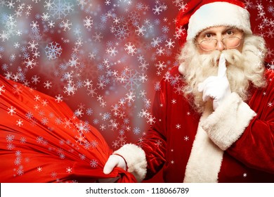 Portrait of Santa Claus with huge red sack keeping forefinger by his mouth and looking at camera - Powered by Shutterstock