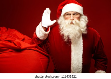 Portrait of Santa Claus raising his hand with huge red sack near by