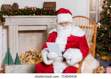 portrait of santa claus using digital tablet while sitting in rocking chair - Powered by Shutterstock