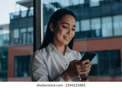 Portrait of satisfied businesswoman using smartphone near expansive window with city view - Powered by Shutterstock