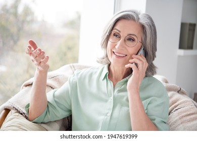 Portrait Of Satisfied Charming Woman Sit On Chair Near Window Speak Phone Hand Palms Explain Toothy Smile Indoors