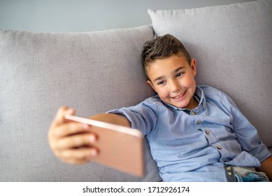 Portrait Of A Satisfied Cheerful Little Boy Holding Mobile Phone And Making Selfie. Funny Small Boy Taking Selfies And Grimacing. Smiling Cute Boy Taking Photos And Facetime Chatting.