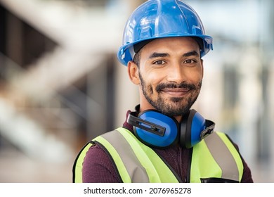 Portrait of satisfied construction site manager wearing safety vest and blue helmet with copy space. Young middle eastern architect watching construction site with confidence and looking at camera. - Shutterstock ID 2076965278