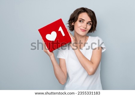 Portrait of satisfied girl with bob hairstyle wear stylish t-shirt look at social media like in hands isolated on gray color background