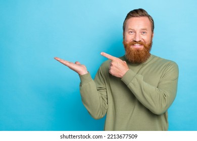 Portrait Of Satisfied Guy With Ginger Hairdo Wear Khaki Pullover Palm Indicating Empty Space Isolated On Turquoise Color Background