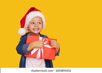 Portrait of a satisfied little child boy in christmas Santa hat. laughing isolated over yellow background. Holds a gift box. Preparing for the New Year holidays - Powered by Shutterstock