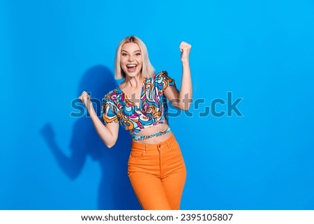 Portrait of satisfied lovely girl wear stylish shirt clenching fists win lottery shout yeah isolated on vivid blue color background