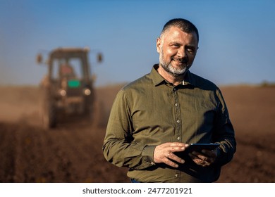 Portrait of satisfied mature farmer standing in field with tablet supervises the cultivation of soil.