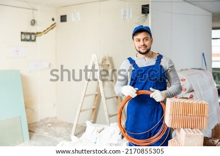 Portrait of satisfied plumber with plastic pipes on his shoulder in a house being renovated