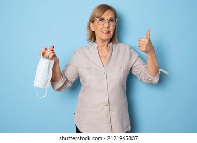 Portrait of satisfied senior woman putting on or taking off medical mask showing thumb up isolated over blue background, copy space. COVID-19 concept. - Powered by Shutterstock