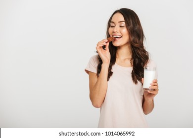 Portrait of a satisfied young asian woman eating cookie and holding glass of milk isolated over white background - Powered by Shutterstock