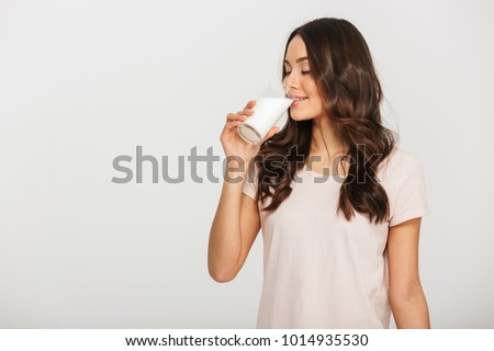 Portrait of a satisfied young asian woman drinking milk from the glass isolated over white background
