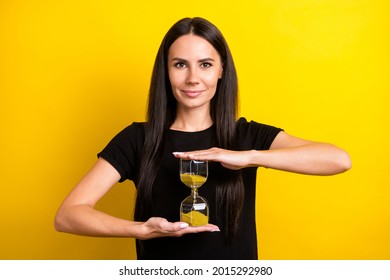 Portrait Of Satisfied Young Lady Smile Hands Hold Sand Clock Look Camera Isolated On Yellow Color Background