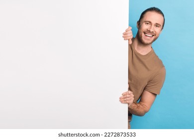 Portrait of satisfied young man beaming smile peeking behind empty space blank isolated on blue color background
