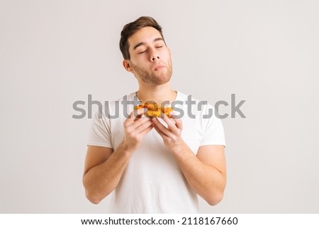 Portrait of satisfied young man with enjoying eating delicious slice of pizza, with closed eyes from pleasure on white isolated background. Studio shot of hungry male student eating tasty food.