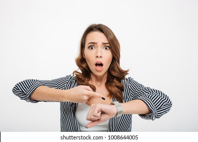 Portrait of a scared casual girl pointing at her wristwatch isolated over white background
