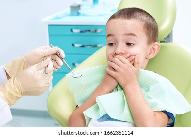 Portrait of a scared child in a dental chair. The boy covers his mouth with his hands, afraid of being examined by a dentist. Children's dentistry - Powered by Shutterstock