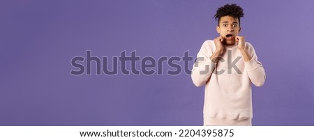 Portrait of scared hispanic guy screaming from fright, hold hands near face, open mouth gasping express fear and terrified emotion from watching horror movie, terrible accident, purple background