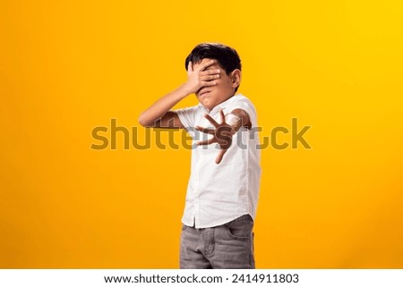 Portrait of scared kid boy showing stop gesure and covering eyes over yellow background.Violence and depression concept