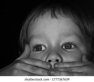 Portrait Of A Scared Little Boy Child. The Kid Covered His Mouth With His Hands. The Concept Of Stuttering, Silence Due To Stress And Shock