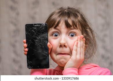 Portrait Of A Scared Little Girl With A Broken Mobile Phone. A Sad Child Broke The Screen Of A Mobile Phone. Cracked Display In Hand Kids. 