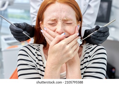 Portrait Of Scared Redhead Female Patient Having Terrible Toothache, Pain, Crying. Cropped Female Dentist Curing Teeth Cavity In Black Gloves, Caries Treatment At Dental Clinic Office. Medicine