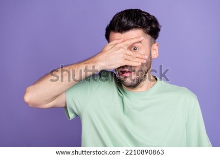 Portrait of scared stressed terrified man with brunet hairdo dressed t-shirt hiding hand cover eye isolated on purple color background