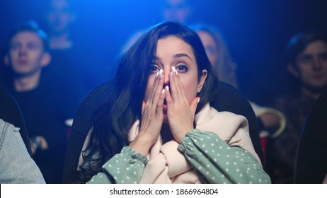 Portrait Of Scared Woman Watching Horror Movie In Dark Hall. Closeup Shocked Girl Closing Face With Hands In Movie Theater. Surprised Female Person Eating Popcorn In Cinema.