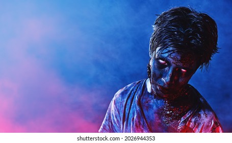 Portrait of a scary zombie boy teenager in blue and crimson smoky lighting. Halloween, horror movie. 