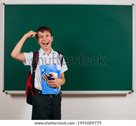 Portrait of a school boy posing with backpack and school supplies, blackboard background - back to school and education concept