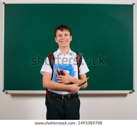 Portrait of a school boy posing with backpack and school supplies, blackboard background - back to school and education concept
