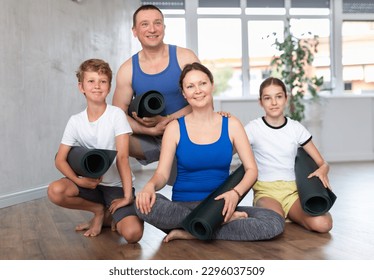 Portrait of school children and their parents holding twisted gym mats, smiling at camera after family yoga training in wellness center - Powered by Shutterstock