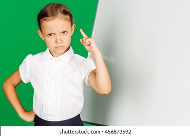 portrait of school girl in a school uniform near whiteboard with wagging her finger. Learning, idea and school concept. Image on green background.
