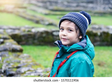 Portrait Of School Kid Explore And Learning About History With School Trip, Happy Child Boy Wearing Hat And Winter Cloths Standing Alone With Blurry Ruins Of Old Abbey Background