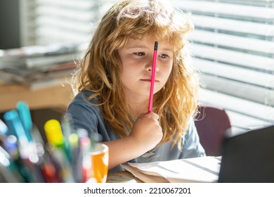 Portrait School Kid Siting On Table Doing Homework. School Boy Making Notes In Copybook During Online Lesson On Laptop At Home. Serious Kid Boy Doing Homework. Child Learning.