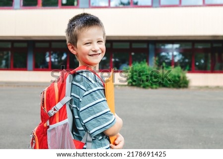 Portrait of a schoolboy boy with a backpack on his back and textbooks in his hands against the school. Back to school. Beginning of the school year