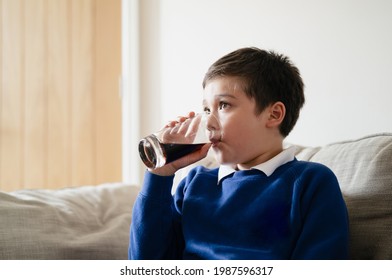 Portrait Schoolboy Drinking Soda Or Soft Drink With Glass,Child Enjoying Cold Fizzy Dink While Watching TV After Back From School,Kid Relaxing At Home In Hot Sunny Day Summer. Unhealthy Food Concept