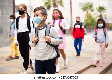 Portrait Of Schoolboy In Medical Mask Standing Near School, Kids On Background
