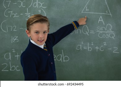 Portrait of schoolboy solving maths formula on chalkboard