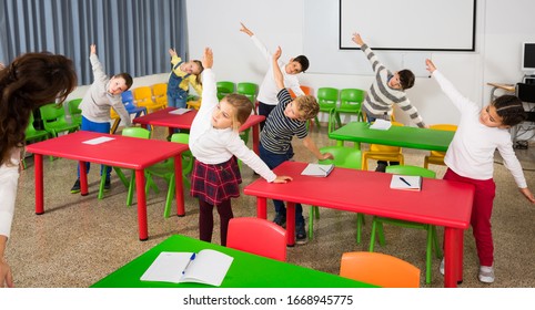 Portrait of schoolchildren with teacher performing daily physical exercises in classroom during break on lesson - Powered by Shutterstock