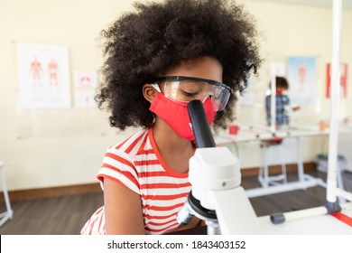 Portrait of a schoolgirl wearing a face mask and looking at the microscope. Education back to school health safety during Covid19 Coronavirus pandemic. - Powered by Shutterstock