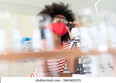 Portrait of a schoolgirl wearing a face mask and looking at the microscope. Education back to school health safety during Covid19 Coronavirus pandemic. - Powered by Shutterstock