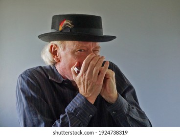 Portrait of seasoned male musician in black wool porkpie hat playing blues harmonica solo.