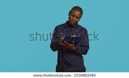 Portrait of security agent holding clipboard, taking notes, receiving orders to secure assigned post, studio background. Guardian maintains logs of observations, handling security breaches, camera B
