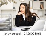 Portrait of seductive female manager in suit sitting at her desktop in office and touching her hair.