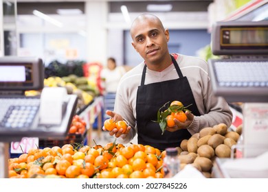 Portrait of a seller in an apron with tangerines near a supermarket counter